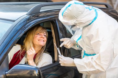 Arabada oturan bir kadın, tıbbi çalışanın COVID-19 testi yapmasını bekliyor. Araba camından burun temizleme örneği alıyor. Coronavirus için PCR testi yapıyor..