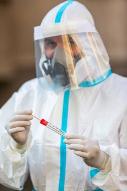 COVID-19 testi yapan bir tıp çalışanı, hastadan alınan burun temizleme örneği için. Koronavirüs için PCR teşhisi, PPE 'deki doktor test kiti tutuyor..