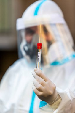 COVID-19 testi yapan bir tıp çalışanı, hastadan alınan burun temizleme örneği için. Koronavirüs için PCR teşhisi, PPE 'deki doktor test kiti tutuyor..