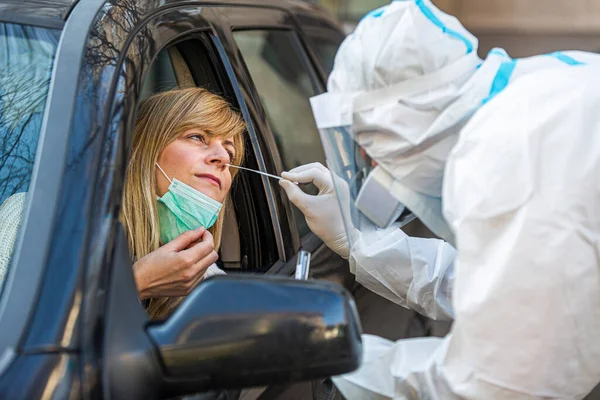 Otomobil sürücüsü COVID-19 testi yapıyor. Kadın hastadan araba camından geniz örneği alıyor. Coronavirus için PCR testi yapıyor..