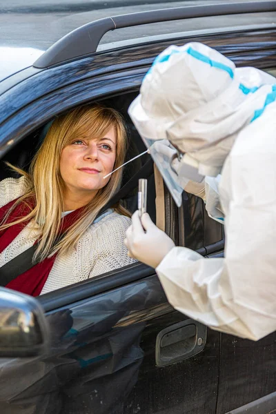 Arabada oturan bir kadın, tıbbi çalışanın COVID-19 testi yapmasını bekliyor. Araba camından burun temizleme örneği alıyor. Coronavirus için PCR testi yapıyor..