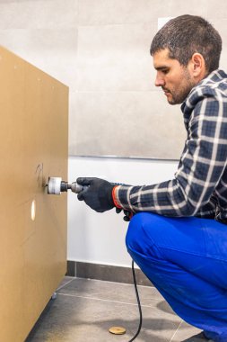 Mutfak raflarında önceden belirlenmiş bir yere yerleştirmeden önce dairesel matkapla delik açan bir marangoz..