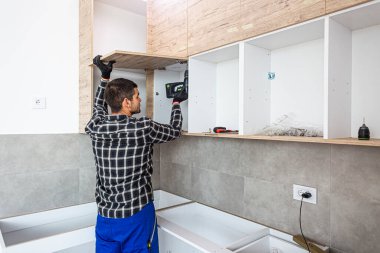 Marangoz mutfak raf kapısının mekanizmalarını (eklemlerini) kurar ve vidalar.