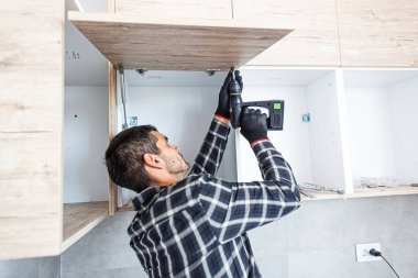 Marangoz mutfak raf kapısının mekanizmalarını (eklemlerini) kurar ve vidalar.