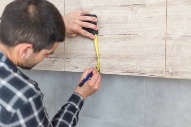 Marangoz, yeni bitmiş mutfak için rafları ve dolapları monte etmeye başladığı boş bir dairede rafları ölçüyordu. Etrafında iş aletleri var..