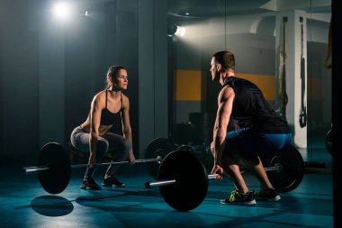 Bir kadın ve bir erkek aynı anda spor salonunda kaldırma egzersizi yapıyor..