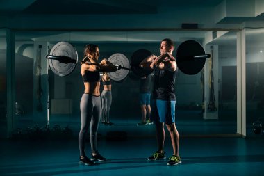 Spor salonunda ağırlıkları üzerinde duran ve halterin ön rafı olarak bilinen egzersiz yapan zinde bir çift..