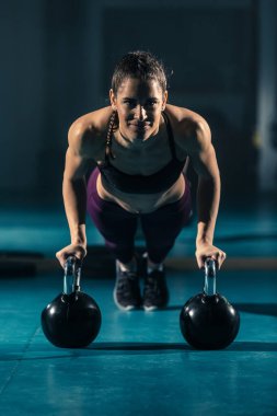 Spor salonunda top şeklinde bir ağırlık olan kettlebell 'in yardımıyla şınav çeken genç bir kadın..