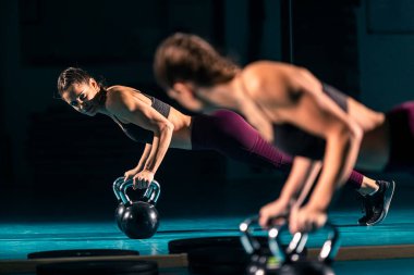 Spor salonunda top şeklinde bir ağırlık olan kettlebell 'in yardımıyla şınav çeken genç bir kadın..