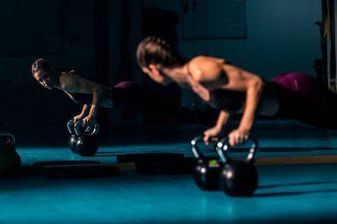 Spor salonunda top şeklinde bir ağırlık olan kettlebell 'in yardımıyla şınav çeken genç bir kadın..