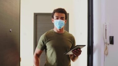 Evin kapısının önündeki yüz maskeli teslimatçı, kağıt bir torba veriyor..