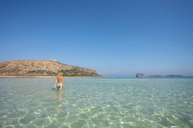 Neşeli kadın denizde sığ sularda yürümekten hoşlanıyor. Girit Adası 'ndaki Balos sahilinin oradaki turkuaz sularda..