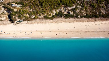 Aerial view of beautiful sandy beach with sunshades and soft turquoise ocean wave. Tropical sea in summer season on Kathisma beach on Lefkada island.