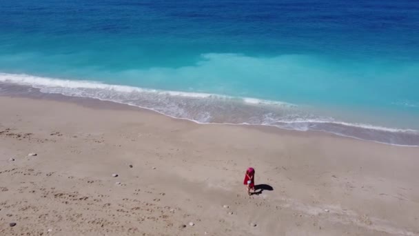 空中俯瞰着身穿红色衣服的女人 她们抱着孩子坐在沙滩上 享受着柔和的绿松石海浪 Lefkada岛上Megali Petra海滩夏季热带海域 — 图库视频影像