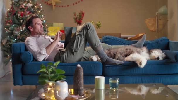 Homem Está Sentado Sofá Sala Estar Com Decorações Natal Acariciando — Vídeo de Stock
