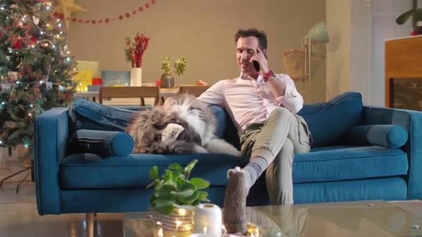 Muž Sedí Gauči Mluví Telefonu Zároveň Hladí Svého Psa Který — Stock video