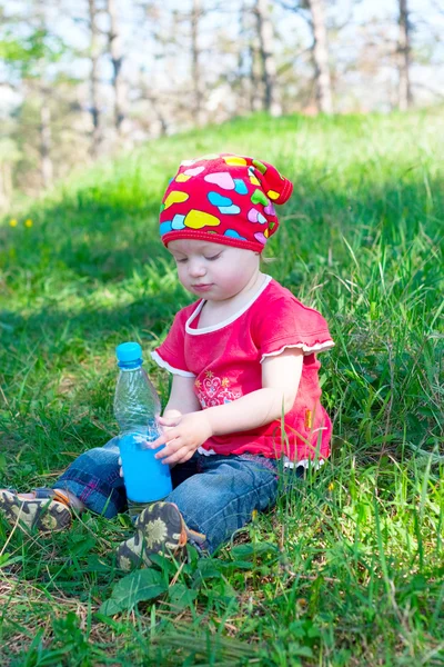 Lilla vackra flicka sitter och innehar en vattenflaska i handen — Stockfoto