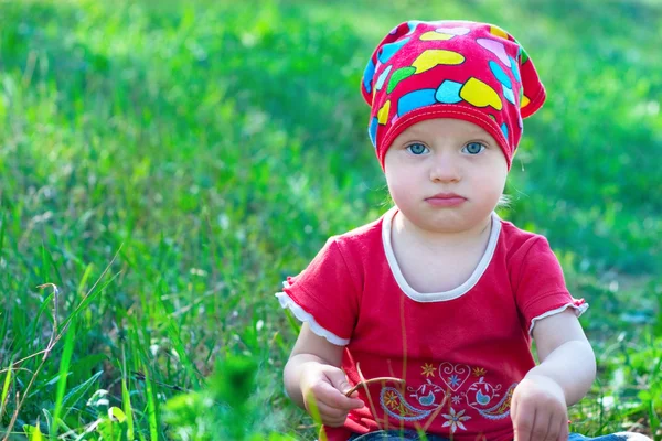 Serious little girl in red clothes sitting in the middle grass — Stock Photo, Image