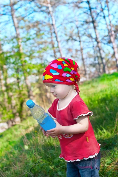 Little beautiful girl in bright clothes holding a bottle in hand — Stock Photo, Image