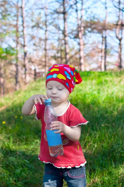 Lilla vackra flicka i ljusa kläder innehar en vattenflaska — Stockfoto