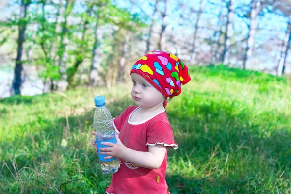 Pequena menina bonita em roupas vermelhas segurando uma garrafa de água — Fotografia de Stock