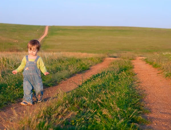 Sweet child in the jeans coverall go to the dirt road — Stock Photo, Image