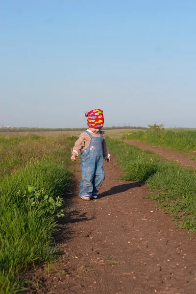 Kind in de jeans coverall en rode bandana Ga naar de onverharde weg — Stockfoto