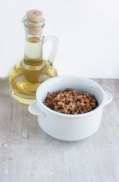 Boiled buckwheat in the white plate and sunflower oil in the gla — Stock Photo, Image