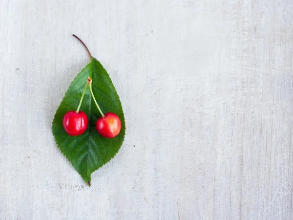 Two red sveet cherry and green leaf on the white board — Stock Photo, Image