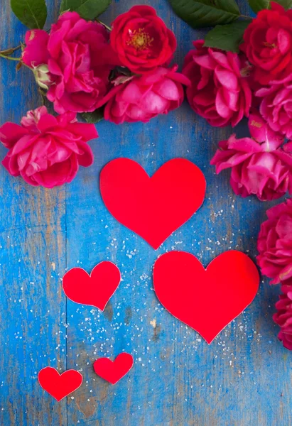 Coeurs et beaucoup de rose rouge sur le panneau de bois bleu — Photo