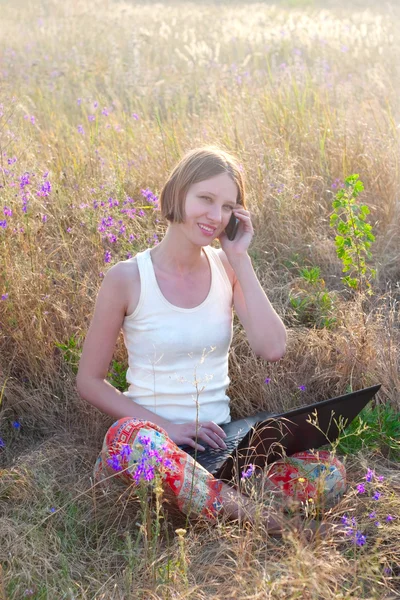 Femme positive avec ordinateur portable et téléphone portable sur la prairie — Photo