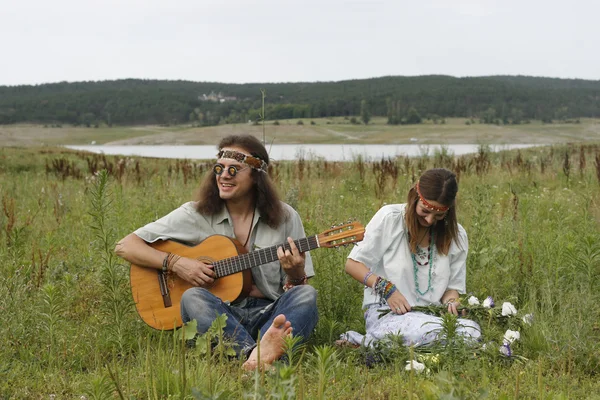 Hippie herrar spelar på gitarr och kvinnan gör en krans — Stockfoto
