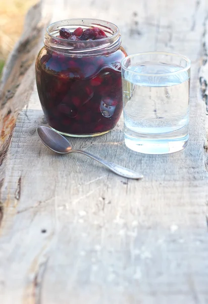 Preserve of berry and tumbler with water — Stock Photo, Image