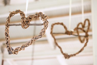 Wooden weaved hearts hanging off roof trusses at wedding, selective focus clipart