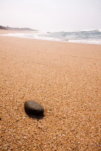 Einzelner schwarzer Felsen am Strand liegend Sand — Stockfoto