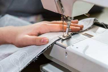 Kadın dikiş makinesiyle dikiş dikiyor. Terzi dükkanında terzi, yakın plan.