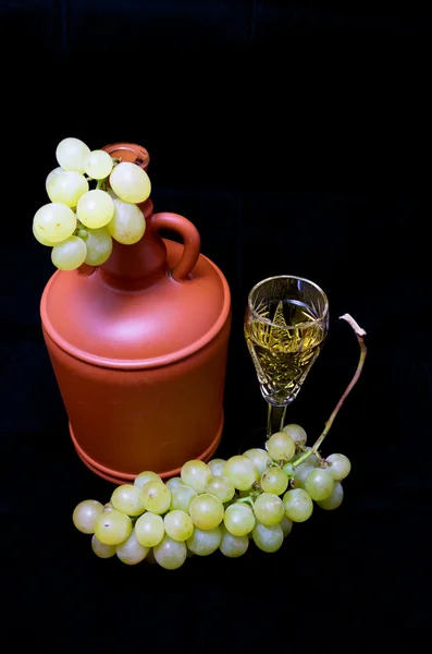 Хрустальный бокал с белым вином, бутылкой и кучей белого винограда на черной ткани — стоковое фото