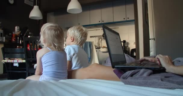 Junge Mutter arbeitet freiberuflich zu Hause via Laptop Kinder sehen Cartoons im Fernsehen — Stockvideo