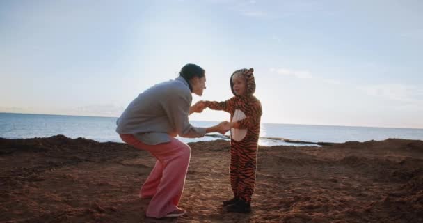 Молодая красивая женщина танцует со своим ребенком купить сына на открытом воздухе на восходе солнца на скалах — стоковое видео