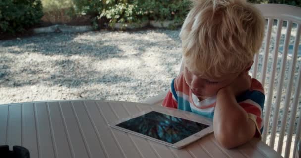 Küçük yorgun çocuk terasta oturan tabletle evden uzaktan öğreniyor. — Stok video