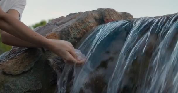 Gros plan bras minces de la jeune femme tirant l'eau de chute d'eau dans la nature — Video
