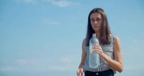 Mujer joven bebiendo agua dulce en el cielo con nubes como fondo en el día soleado — Vídeos de Stock