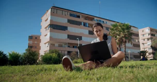 Dışarıda dizüstü bilgisayarla çalışan genç ve güzel bir kadın parkta oturuyor. — Stok video