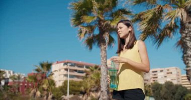 Genç ve çekici bir kadın güneşli bir günde açık hava şişesinden su içer.