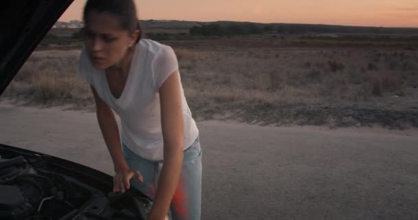 Droevige vrouw staat voor aan kapotte auto en met behulp van de smartphone om service te vinden — Stockvideo