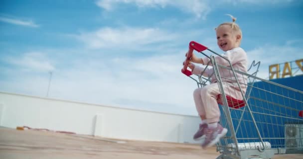 Мила дівчинка сидить і посміхається в супермаркеті кошик на відкритому повітрі — стокове відео