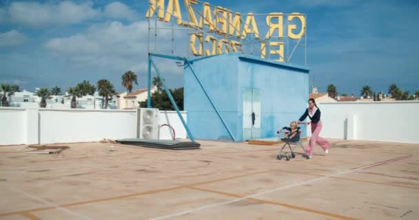 Νεαρή ευτυχισμένη μητέρα τρέχει με καλάθι αγορών με το παιδί κάθεται σε αυτό στο πάρκινγκ — Αρχείο Βίντεο