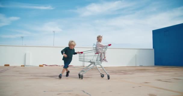 Kinderen hebben plezier spelen met supermarkt sopping kar in de buitenlucht parkeren — Stockvideo