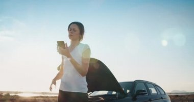 Arızalı aracın önündeki genç kadın yolda akıllı telefon servisini kullanıyor.