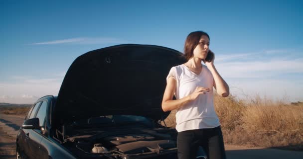 Mujer joven en frente de coche de avería utilizando el servicio de llamadas de teléfonos inteligentes en la carretera — Vídeos de Stock